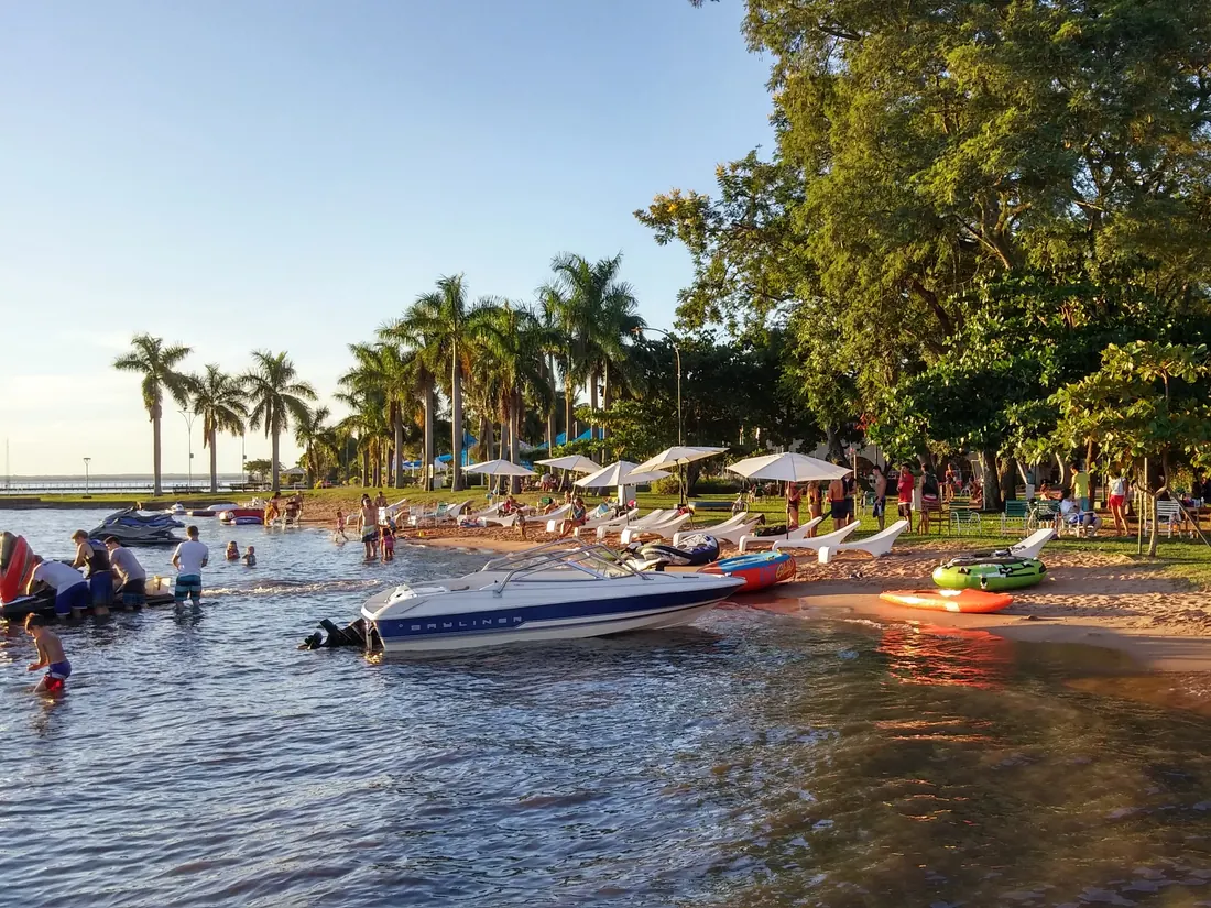 Beach on Lake Ypacaraí in San Bernardino, with boats on the shore and palm trees